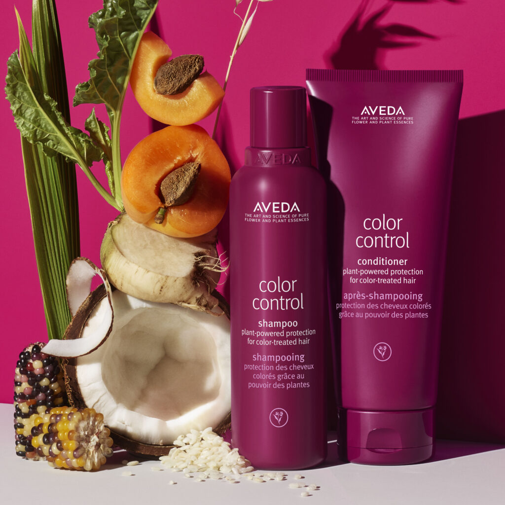 Aveda Color Control shampoo and conditioner bottles are displayed alongside fruits and vegetables against a magenta background.