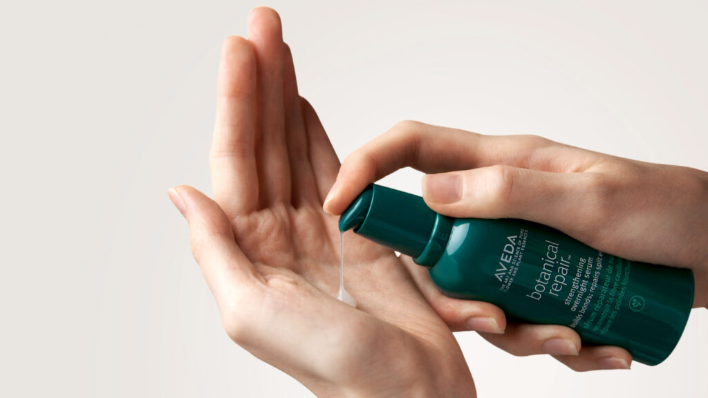 A person is dispensing Aveda botanical repair product onto their palm.