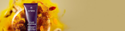 Aveda Invati Advanced hair treatment tube displayed in front of a blurred yellow floral and spice background—perfect for winter hair care and holiday hair prep.